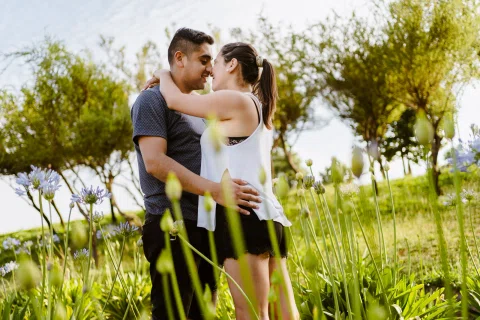 Hombre y mujer se abrazan entre plantas altas en un jardín.
