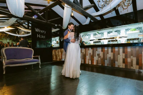 Hombre con traje azul y mujer con vestido blanco se abrazan frente a una barra.