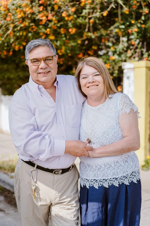 Hombre y mujer permanecen abrazados frente a un jardín con flores.