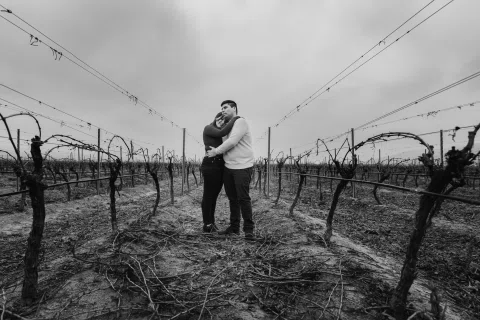 Hombre y mujer se abrazan entre viñas en una fotografía en blanco y negro.