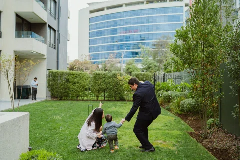 Hombre con traje oscuro y mujer de chaqueta clara están agachados junto a un niño pequeño sobre el césped.