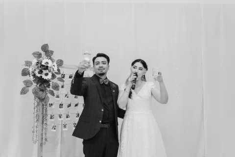 Hombre y mujer alzan copas; ella sostiene además un micrófono, en una fotografía en blanco y negro.