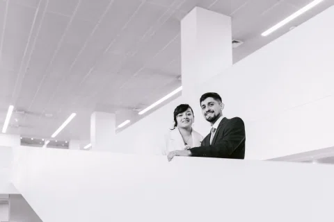 Hombre y mujer se asoman por un borde interior del edificio, vistos desde abajo en una fotografía en blanco y negro.