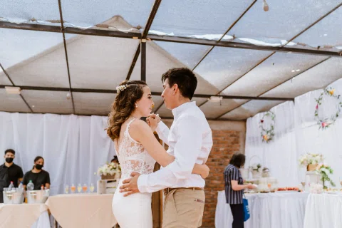 Hombre con camisa blanca y mujer con vestido blanco bailan abrazados bajo una carpa.