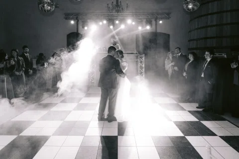 Hombre y mujer bailan abrazados entre humo escénico en una fotografía en blanco y negro.