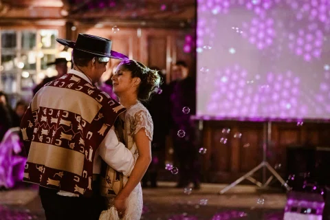 Hombre con poncho y sombrero y mujer con vestido blanco bailan juntos entre luces de colores y burbujas.