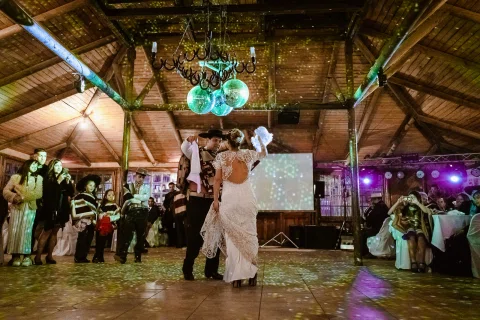 Hombre con poncho y sombrero baila con una mujer de vestido blanco que sostiene un pañuelo blanco en alto dentro de un salón.