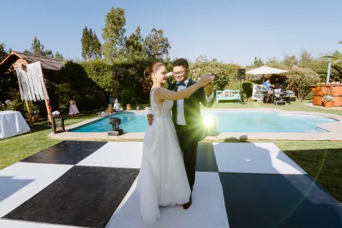 Hombre con traje azul y mujer con vestido blanco bailan juntos sobre la pista exterior junto a la piscina.