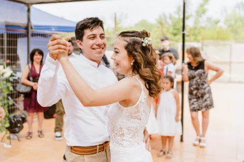 Hombre con camisa blanca y mujer con vestido blanco bailan tomados de las manos, con otras personas detrás.