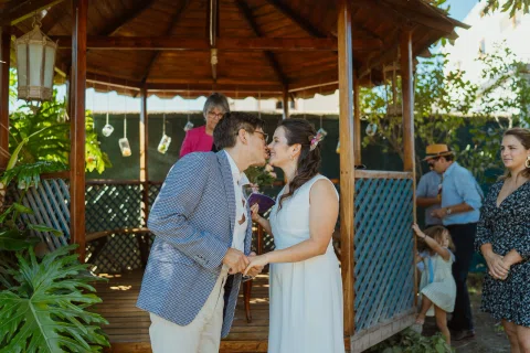 Hombre y mujer se besan junto a un gazebo mientras se toman de las manos.