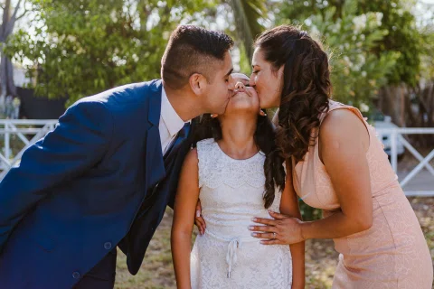 Hombre y mujer besan las mejillas de una niña que se encuentra entre ambos.