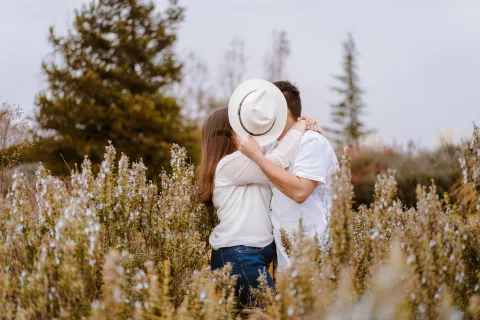 Hombre y mujer se besan mientras un sombrero blanco cubre parcialmente sus rostros.
