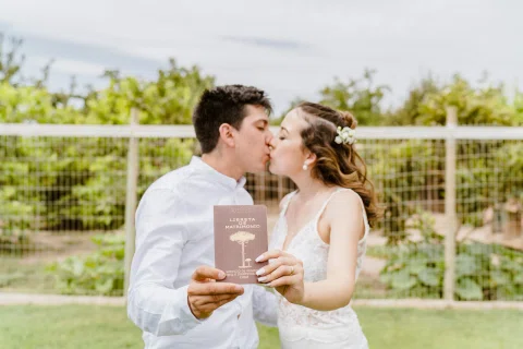 Hombre y mujer se besan mientras sostienen frente a la cámara una libreta de matrimonio.