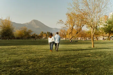 Hombre y mujer caminan de espaldas por un parque con montañas al fondo.