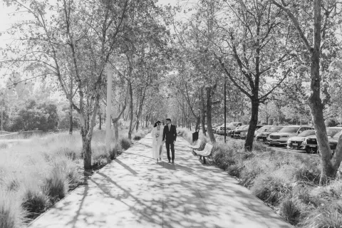 Hombre y mujer caminan juntos por un sendero entre árboles, en una fotografía en blanco y negro.