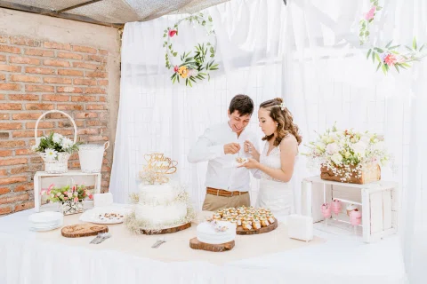 Hombre con camisa blanca y mujer con vestido blanco comen de un pequeño plato frente a una mesa con torta y postres.