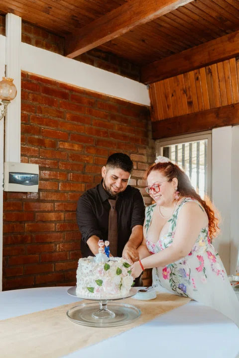 Hombre con camisa negra y mujer de cabello rojo cortan una torta juntos.