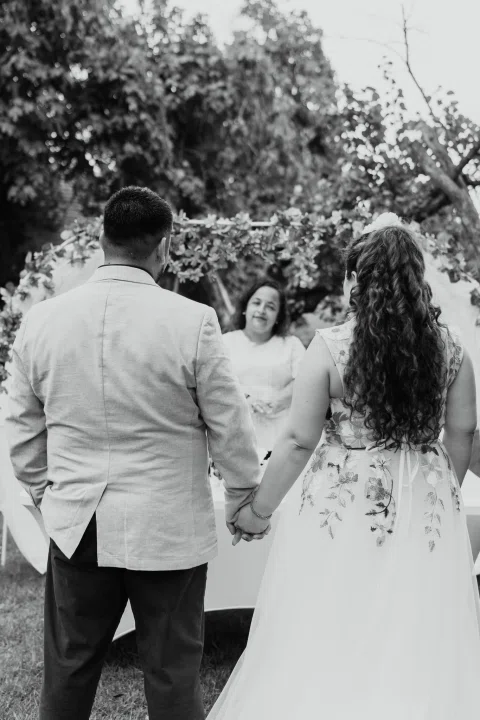 Hombre con chaqueta clara y mujer de cabello rojo permanecen de espaldas frente a una mujer con vestido blanco, en una fotografía en blanco y negro.