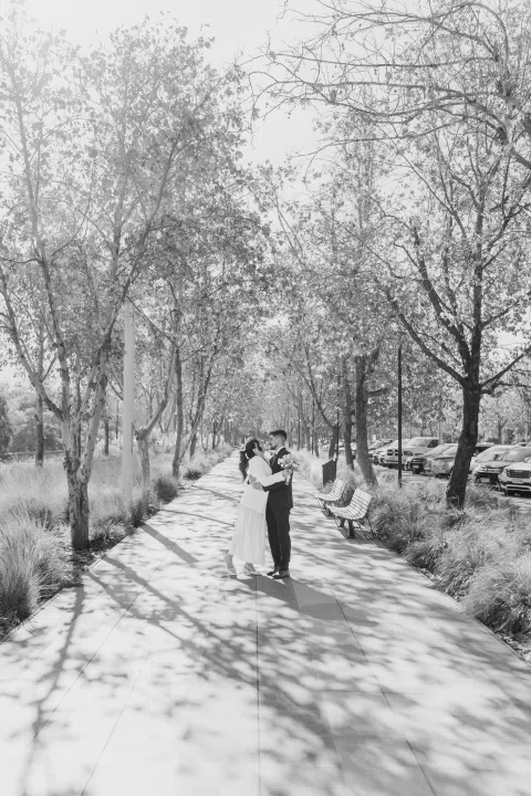 Hombre y mujer aparecen a distancia sobre un sendero entre árboles, en una fotografía en blanco y negro.