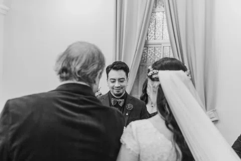 Hombre con traje oscuro y mujer con vestido blanco frente a un tercer hombre de espaldas, en una fotografía en blanco y negro.