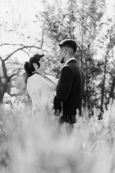 Hombre y mujer permanecen juntos entre flores y vegetación, en una fotografía en blanco y negro.