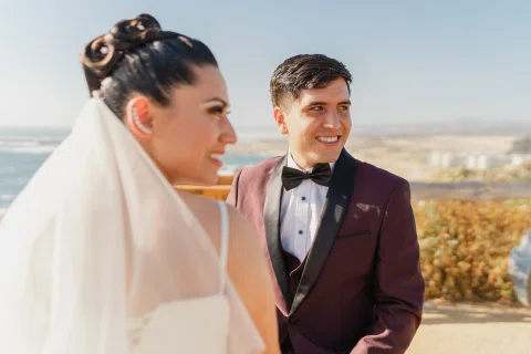 Hombre y mujer están juntos al aire libre con un paisaje costero al fondo.