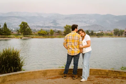 Hombre y mujer están juntos frente a una laguna con montañas al fondo.