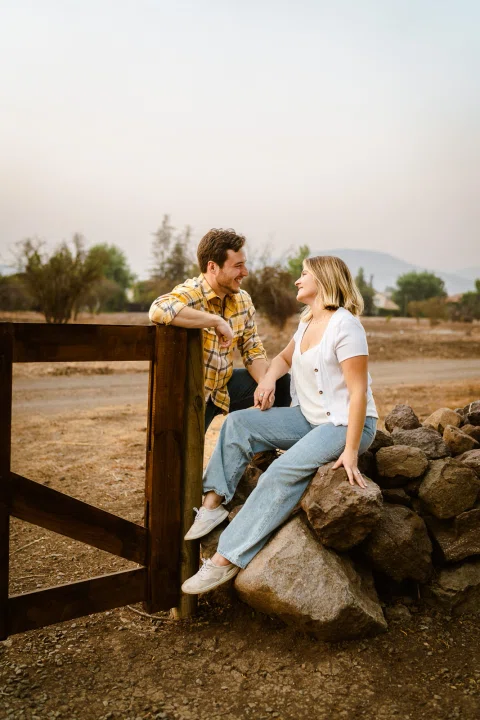 Hombre y mujer están juntos junto a una baranda de madera y unas piedras, cerca del agua.