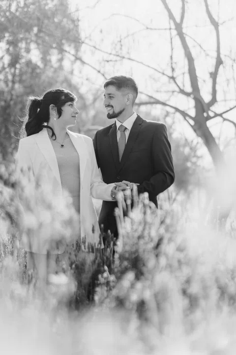 Hombre y mujer permanecen juntos con las manos unidas entre flores, en una fotografía en blanco y negro.