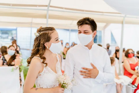 Hombre y mujer con mascarillas permanecen de pie uno junto al otro bajo una carpa.