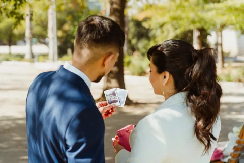 Hombre con traje azul y mujer con traje claro miran fotografías instantáneas; ella sostiene una cámara rosada.