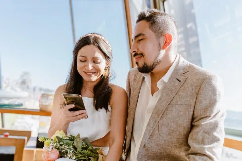 Hombre y mujer miran un teléfono juntos mientras ella sostiene un ramo de flores.
