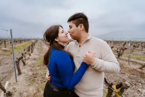 Hombre y mujer permanecen frente a frente tomados de las manos entre hileras de viñas.