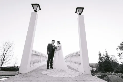 Hombre y mujer posan a distancia entre dos pilares sobre un puente blanco, en blanco y negro.
