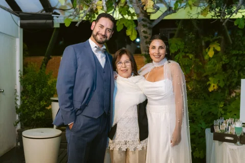 Hombre con traje azul y mujer con vestido blanco posan junto a una mujer con chaqueta negra.