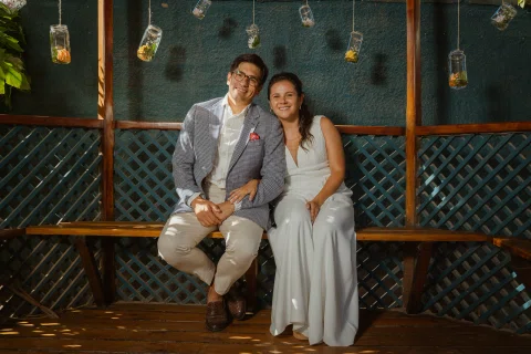 Hombre y mujer posan sentados juntos en una banca dentro de un gazebo.
