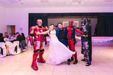 Hombre con traje azul y mujer con vestido blanco posan junto a tres personas con disfraces de distintos colores.