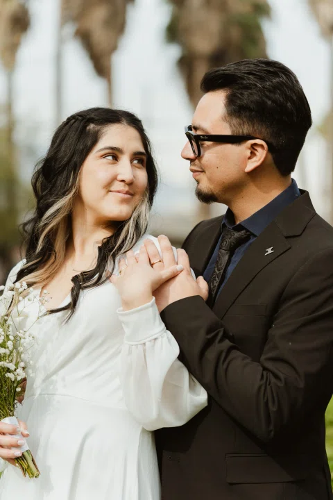 Hombre y mujer posan juntos en primer plano junto a un ramo de flores.