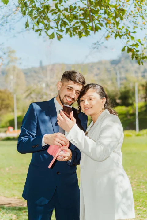 Hombre con traje azul y mujer con traje claro revisan juntos una fotografía instantánea mientras sostienen una cámara rosada.