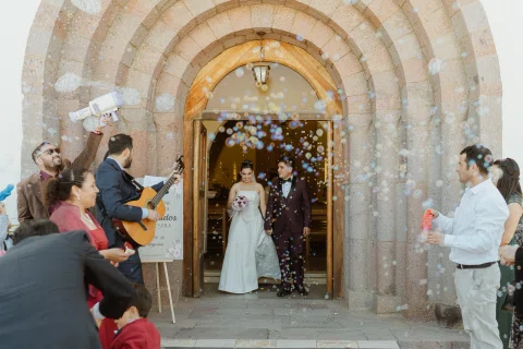 Hombre y mujer salen por la puerta de piedra de una iglesia mientras hay burbujas alrededor.