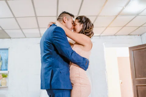 Hombre y mujer se abrazan estrechamente dentro de un espacio interior.