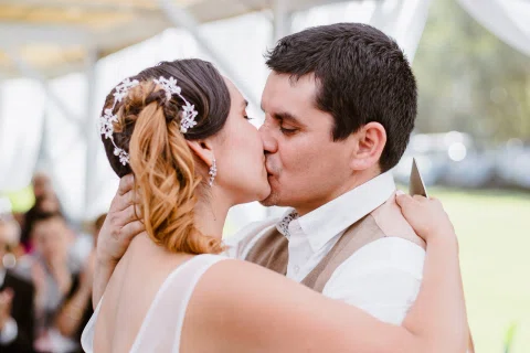 Hombre y mujer se besan de perfil al aire libre.