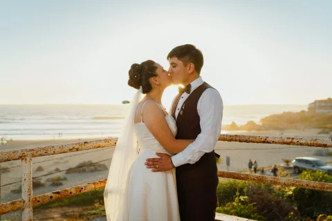 Hombre y mujer se besan frente a la costa con luz de atardecer.