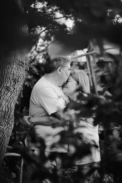 Hombre y mujer se besan entre hojas desenfocadas, en una fotografía en blanco y negro.