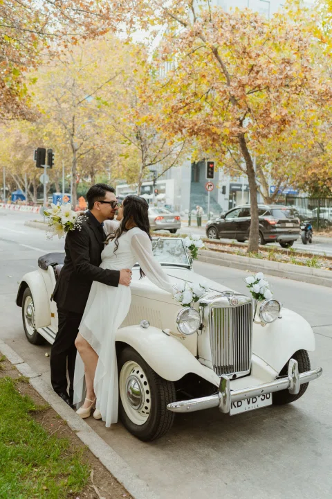 Hombre y mujer se besan junto a un automóvil convertible blanco decorado con flores.