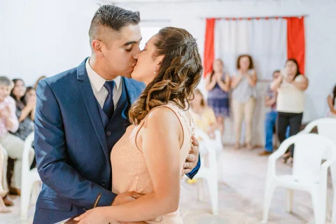 Hombre y mujer se besan mientras varias personas aparecen al fondo.