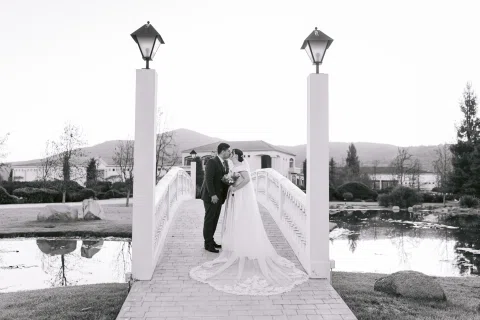 Hombre y mujer se besan sobre un puente blanco en una fotografía en blanco y negro.