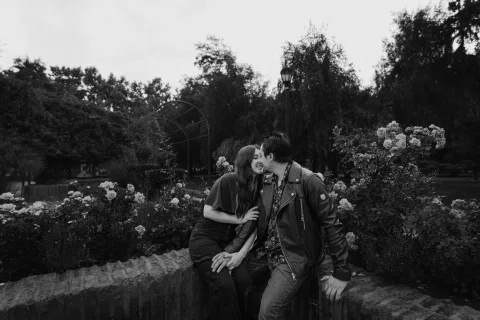 Hombre y mujer se besan mientras están sentados en un jardín en una fotografía en blanco y negro.