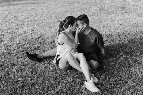 Hombre y mujer se besan sentados sobre el césped en un encuadre horizontal en blanco y negro.