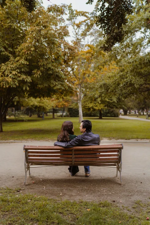 Hombre y mujer están sentados en una banca del parque vistos de espaldas.